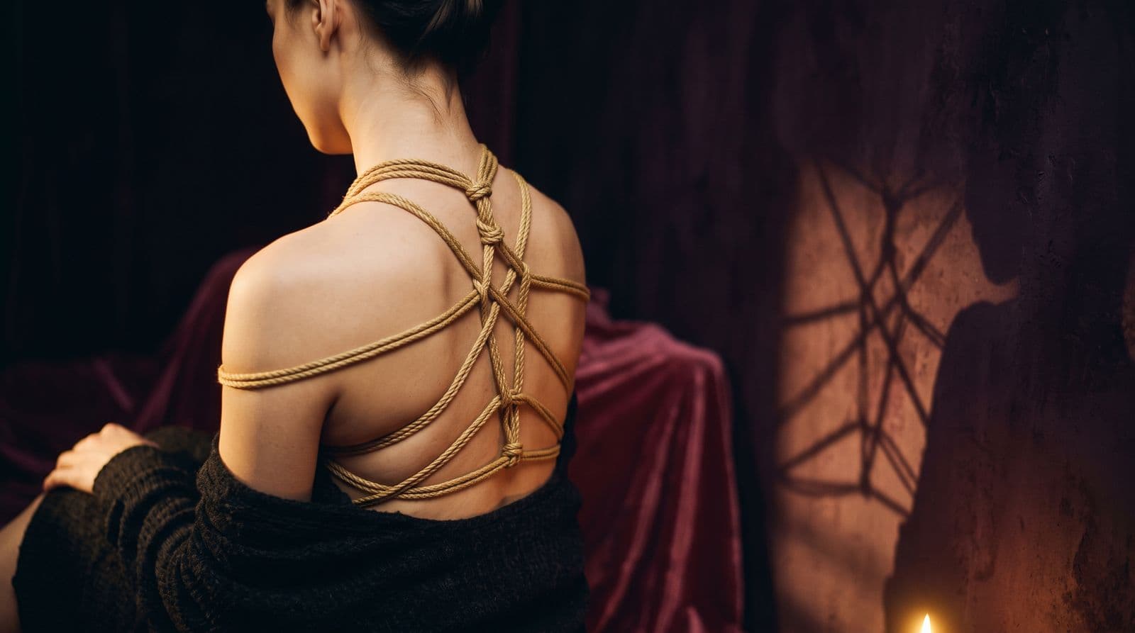 Motif de corde shibari tracé sur une épaule dans une lumière tamisée dorée
